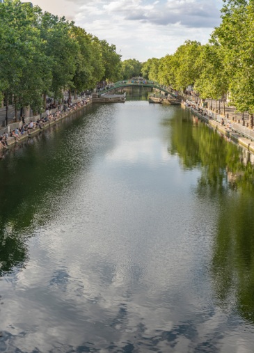 Canal bordé d’arbres avec promenade, pont piéton et ambiance urbaine paisible